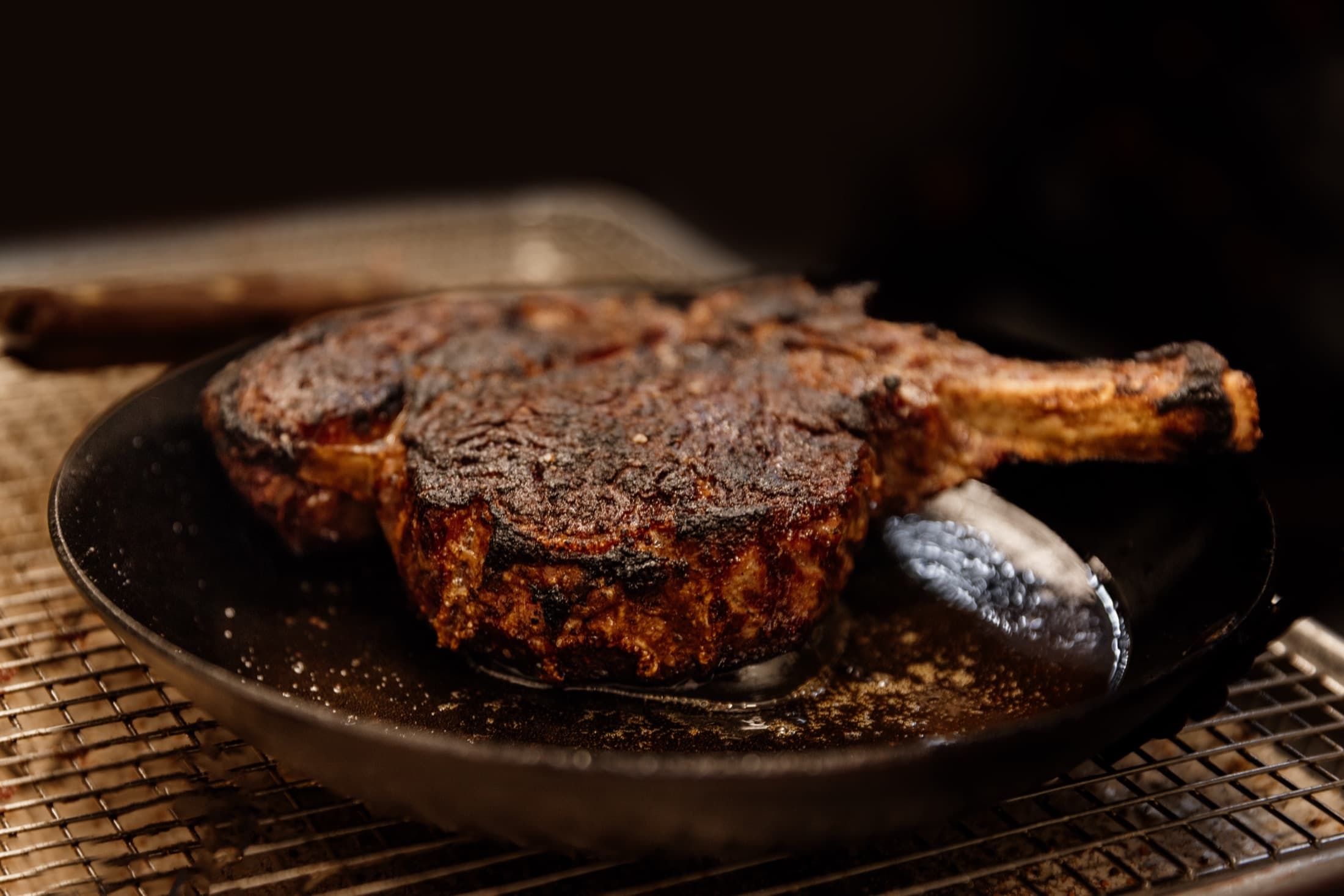 Dry-aged tomahawk steak searing in a cast iron pan at CHR Steak